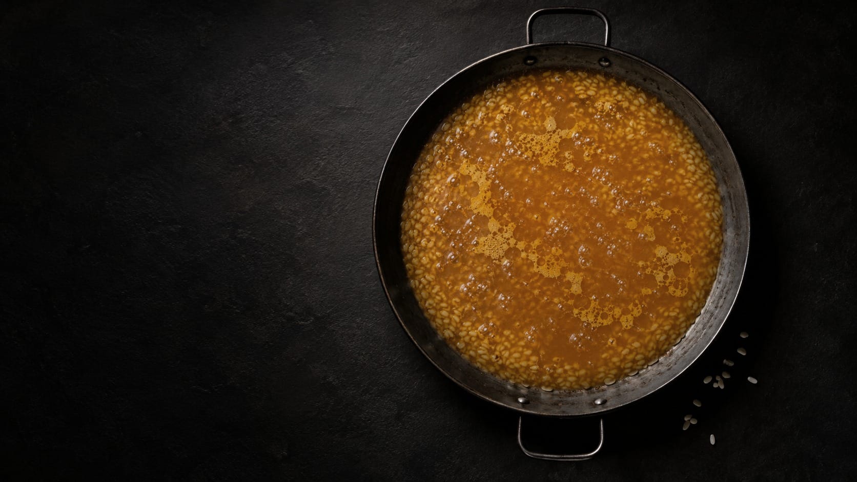 Imatge d'ambient creada amb IA: la paella plena d'un brou daurat que cobreix l'arròs, vista des de dalt.