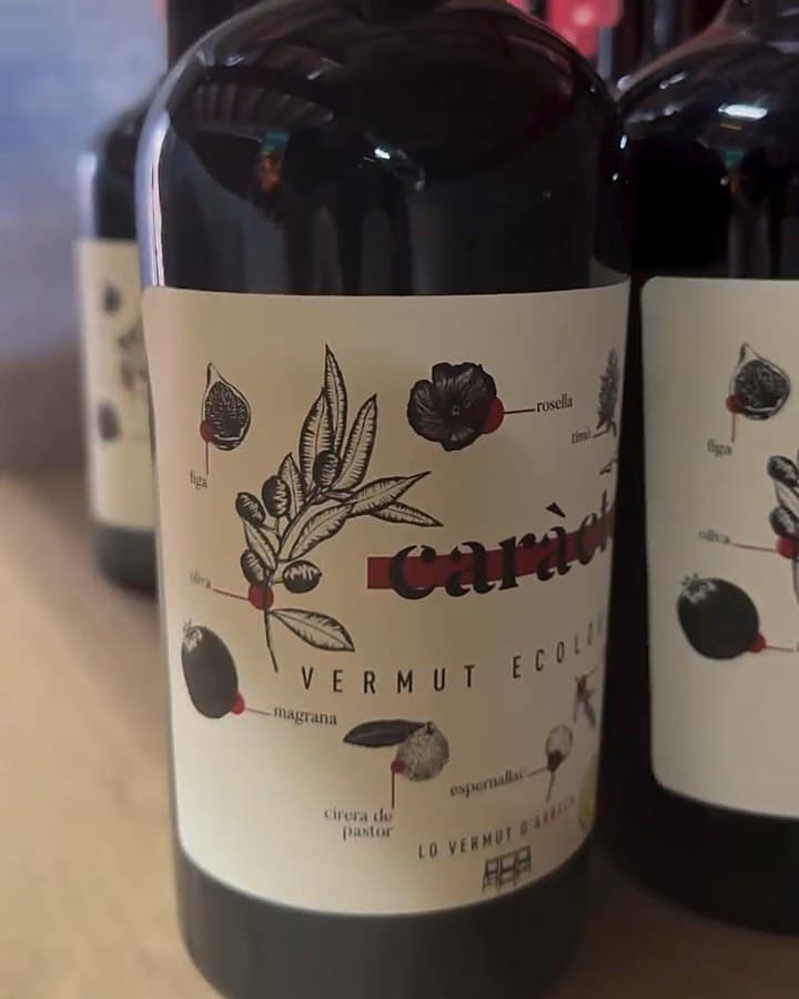 Ampolles fosques de vermut en un prestatge de l'obrador, amb una etiqueta il·lustrada amb oliva, figa, magrana i rosella.