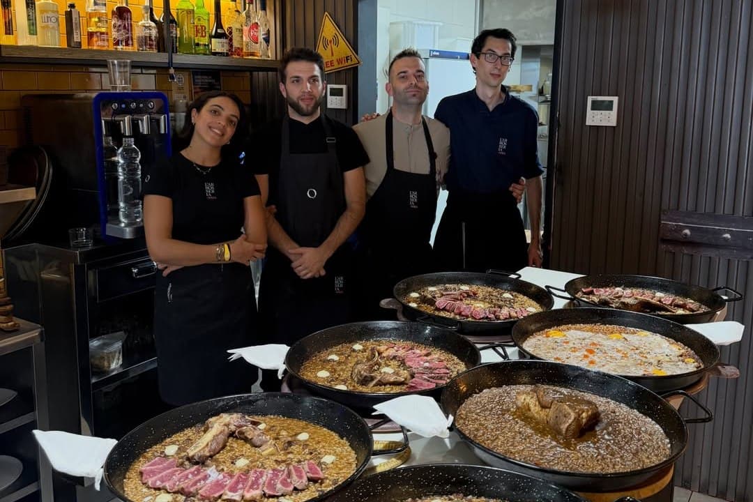 Ramon Tudela i tres persones de l'equip darrere la barra, amb paelles d'arròs acabades repartides pel taulell.